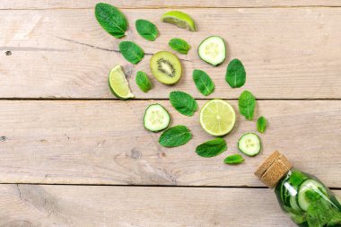 Limonlu su şişesi ve ahşap masada nane. Limonlu su, salatalık ve ahşap zemin üzerinde nane. Yaz içkisi. Taze meyve sanatı. Orijinal yaz taze kokteyli..