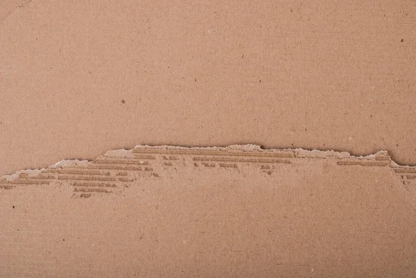 Old textured cardboard sheet with torn edges. Brown cardboard torn off. Cardboard texture. A sheet of tattered cardboard lies on a whole sheet of cardboard.