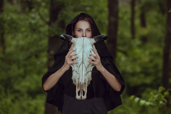 Victim with skull of the animal instead of head. Photo stylized as shooting on an old camera, with noise and imperfection of the image. Woman in forest with skull of cow occupies Occult calls to demon