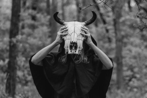Victim with skull of the animal instead of head. Photo stylized as shooting on an old camera, with noise and imperfection of the image. Woman in forest with skull of cow occupies Occult calls to demon