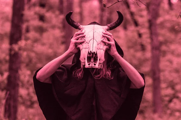 Victim with skull of the animal instead of head. Photo stylized as shooting on an old camera, with noise and imperfection of the image. Woman in forest with skull of cow occupies Occult calls to demon