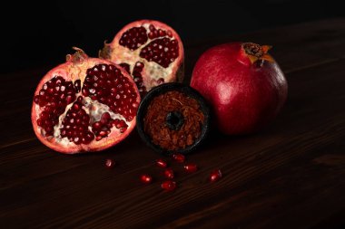 Kırmızı nar aromalı tütünle dolu nargile tütünü bir bütünün yanında duruyor ve koyu kahverengi ahşap zemin üzerinde nar kesiyor. Nargile iç.