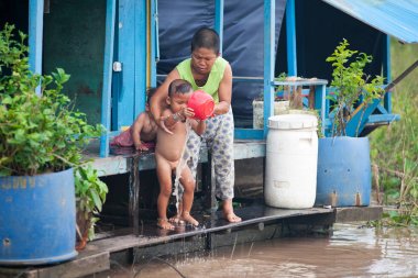 Aile Tonle Sap Gölü bir teknede yaşıyor. Anne çocuğunu yıkar. Kamboçya. 31 Temmuz 2012