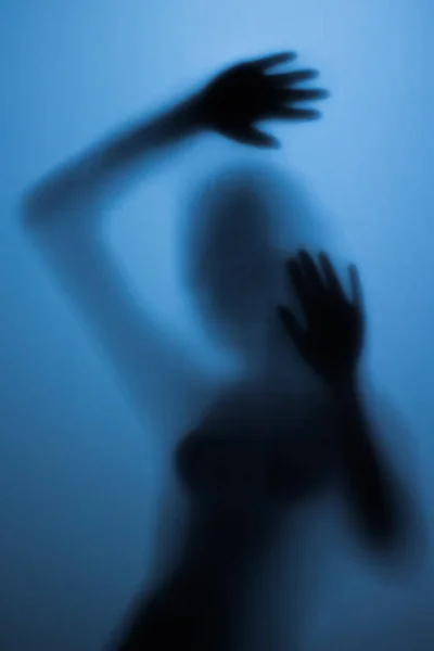 Gruselige Silhouette eines Mädchens hinter einem Glas im Badezimmer.Gruseliges Mädchen hinter der Glastür im blauen Licht — Stockfoto