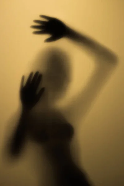 Korkunç silueti banyoda bir cam arkasında bir kız. Sarı ışıkta cam kapının arkasında korkunç kız