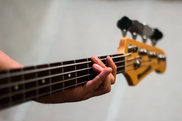 Bass guitar in playing musician hands close-up. Focus on bass guitar neck in player hands. Unrecoginzable bass guitar player performing at music studio, blurred background