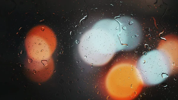 Droppar av regn rinna ner glaset mot bokeh bakgrund av rörliga bilar — Stockfoto