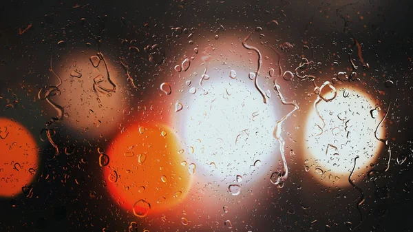Droppar av regn rinna ner glaset mot bokeh bakgrund av rörliga bilar — Stockfoto