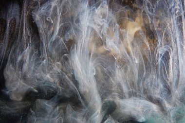 Soyut bronz boya, suda farklı renkte boyalarla yavaş çekimde karıştırılmış. Su altında dönen mürekkepli bulut. Soyut duman patlaması