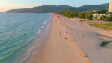 PHUKET, THAILAND - 15 MAR 2020: Karon sahilinde gün batımı, insanlar denizde yüzer ve güneşlenir, tatil köyü kumsalı. Karantina covid-19 nedeniyle plajları kapatmadan birkaç gün önce. Hava 4k görüntüsü