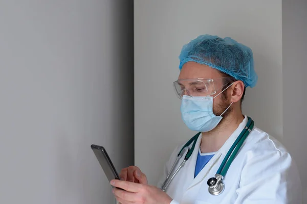 Médico en mascarilla usando smartphone en el hospital —  Fotos de Stock