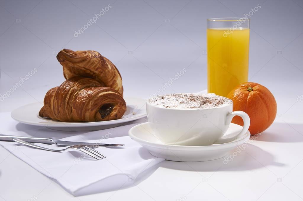 Fresh croissants, orange juice, coffee and oranges. Continental breakfast on white table