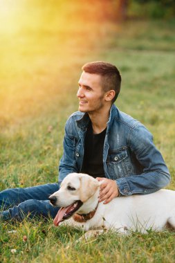 İnsan ve köpek labrador çimenlerin üzerinde günbatımında oturur.
