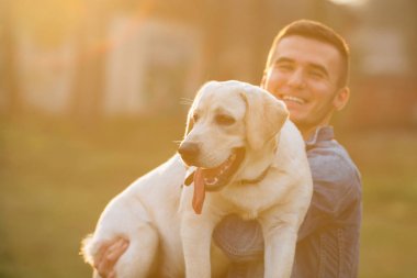 Mutlu bir adam onun köpek labrador günbatımında parkta elinde tutan. Tonda fotoğraf