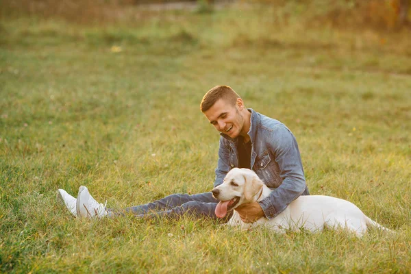 Glückliche Freunde Mann und Hund Labrador sitzen auf Gras im Park bei Sonnenuntergang. getöntes Foto — Stockfoto