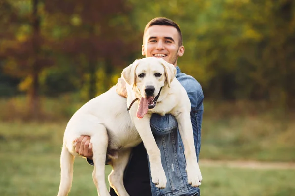 Retrato del hombre feliz sosteniendo al perro Labrador en las manos en el parque — Foto de Stock