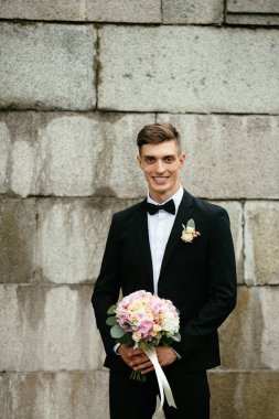 Bir buket çiçek beton duvara bir arka plan üzerinde tutan şık gülümseyen gelin. Düğün günü.