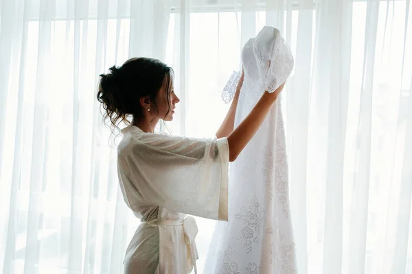 Esküvői. Gyönyörű menyasszony tart esküvői ruha a kezét. A menyasszony esküvője napján reggel. — Stock Fotó