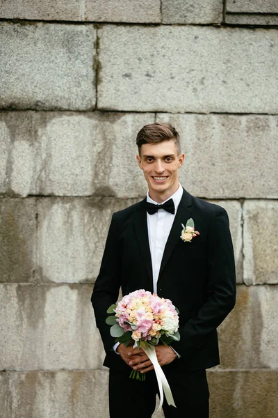 Elegante novia sonriente sosteniendo un ramo de flores sobre un fondo de una pared de hormigón. Día de la boda . — Foto de Stock