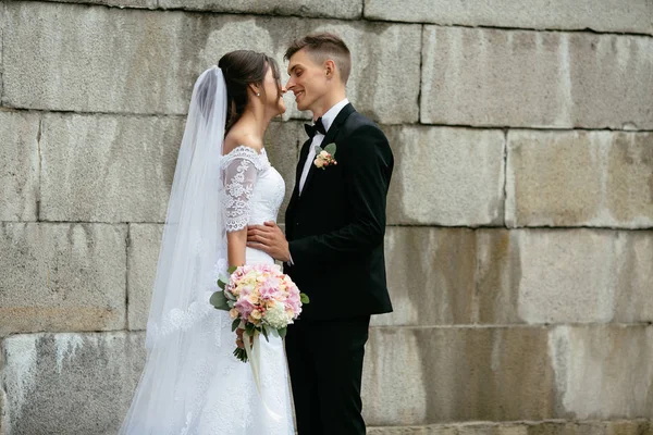 Casamento. Retrato de noiva feliz e noivo olhando um para o outro no fundo de uma parede de concreto. Dia do casamento . — Fotografia de Stock