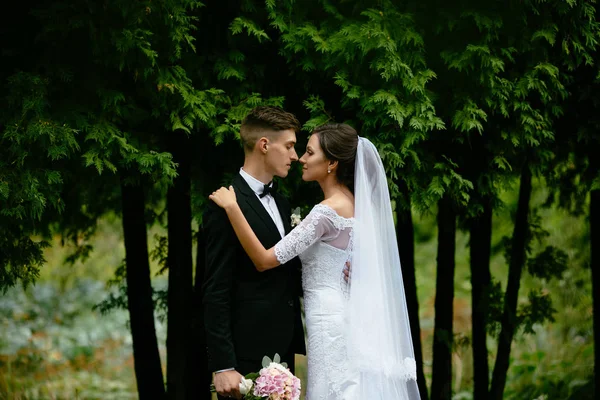 Bröllop. Vackra brud omfamnar brudgummen medan han håller en bukett i sin högra hand. — Stockfoto