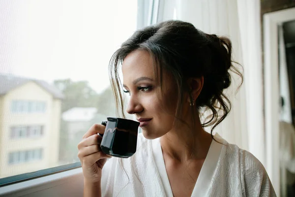 Hermosa chica tomando café temprano en la mañana en el alféizar . — Foto de Stock