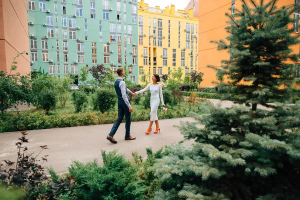 Novia y novio caminando en el día de la boda en el colorido fondo del edificio —  Fotos de Stock