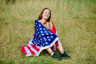 Mutlu kız Amerikan bayrağı ile çimlerde oturuyor