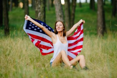 Mutlu kız Amerikan bayrağı ile çimlerde oturuyor