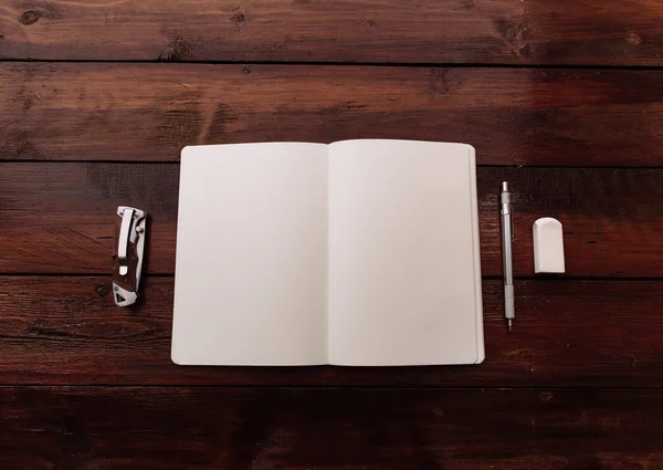Cuaderno abierto con peneraser y cuchillo en un escritorio de madera - Mock up — Foto de Stock