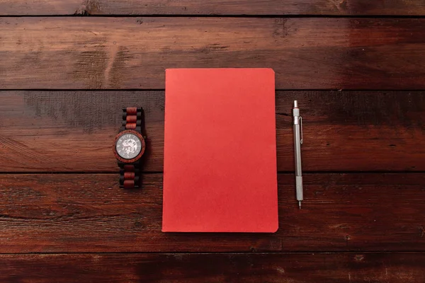 Cuaderno rojo con relojes de pluma y muñeca en un escritorio de madera - Mock up — Foto de Stock