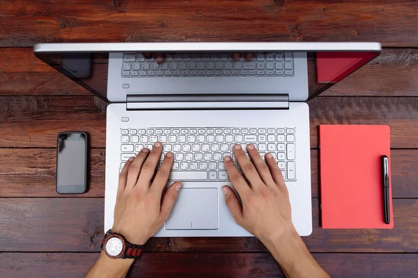 Laptop na vintage drewniany stół z telefonu komórkowego, Notatnik i długopis. Ręce człowieka za pomocą laptopa - widok z góry. — Zdjęcie stockowe