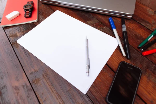 Lugar de trabajo, hoja de papel en blanco con lápices de colores, teléfono móvil, portátil y reloj de pulsera sobre un fondo de madera - Mock up — Foto de Stock