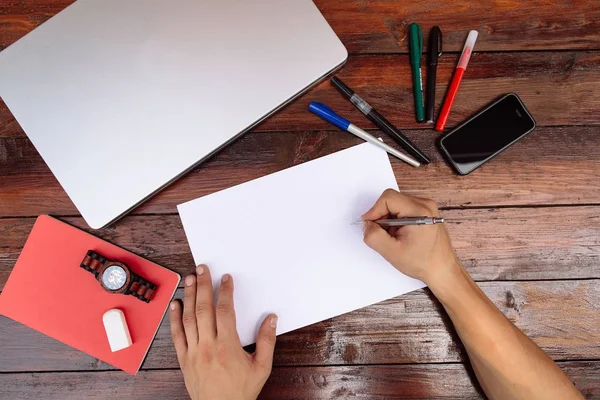 Lugar de trabajo, la mano está dibujando en la hoja blanca. Dibujo a mano sobre una hoja de papel en blanco con lápices de color sobre un escritorio de madera. — Foto de Stock