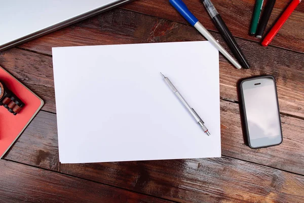 Lugar de trabajo, hoja de papel en blanco con lápices de colores, teléfono móvil, portátil y reloj de pulsera sobre un fondo de madera - Mock up — Foto de Stock