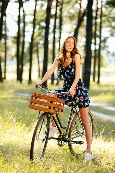 Chica feliz en una bicicleta con una cesta en el bosque . — Foto de Stock