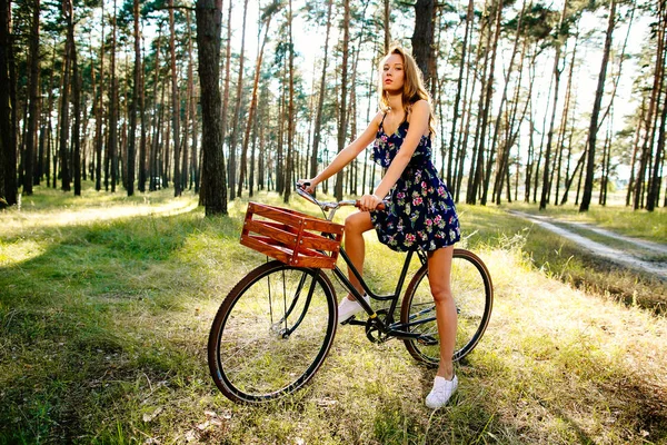 Glückliches Mädchen auf einem Fahrrad mit einem Korb im Wald. — Stockfoto