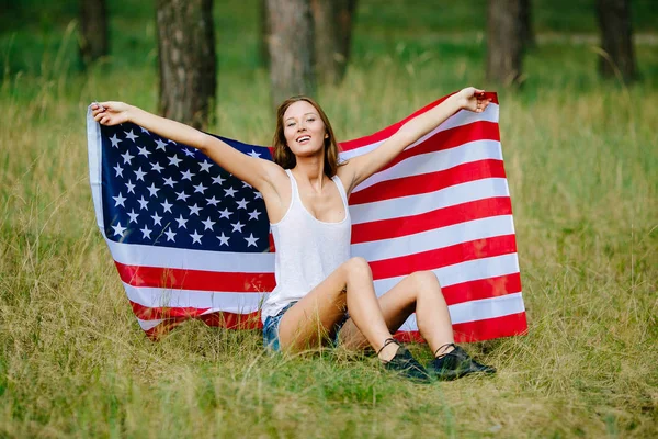 快乐的女孩坐在草地与美国国旗上 — 图库照片