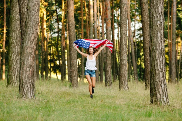 Girl in shorts running with American flag in hands.