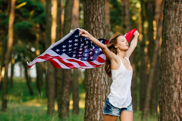Girl in shorts running with American flag in hands.