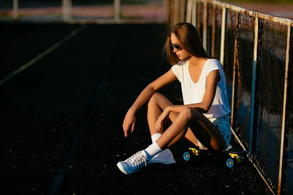 Een sexy vrouw ziet er beneden zittend op haar skateboard. — Stockfoto