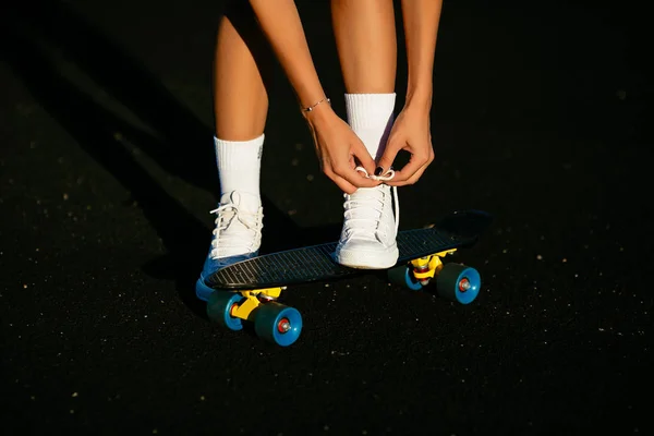 Dívka, vázání její bílé boty poblíž skateboard. — Stock fotografie