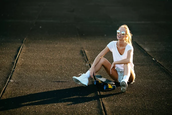 Krása leží na skateboardu na západ slunce. — Stock fotografie