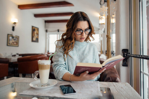 Девушка в очках читает детективную книгу в кафе
