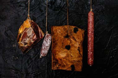 Variety meat delicacies. Sticks of smoked salami, prosciutto crudo, smoked bacon and dry-cured sausages hanging from hooks clipart