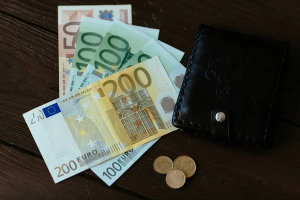 Wallet and Euro cash. Brown male wallet and euro banknotes with euro cents on wooden background