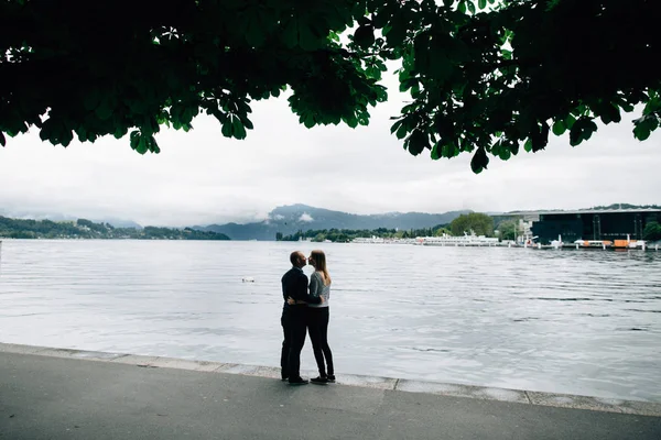 Hermosa pareja besándose en el paseo marítimo con paisaje de montaña —  Fotos de Stock