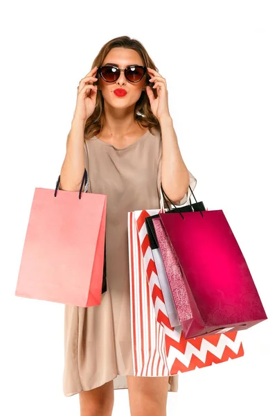 Nő visel, napszemüveget, jelentő-bevásárló táskák, és nézte a kamera fölött fehér elszigetelt háttér. — Stock Fotó