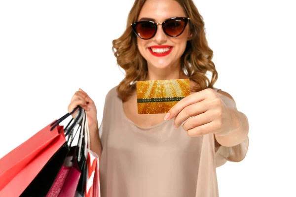 Jovem morena feliz em óculos de sol segurando cartão de crédito de ouro e sacos de compras coloridos — Fotografia de Stock
