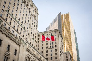 Canadian flag in front of a business building and an older skyscraper in Toronto, Ontario, Canada clipart
